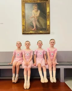 Royal Academy of Dance Exam Success 2025 - 4 young ballerinas sit beneath a painting