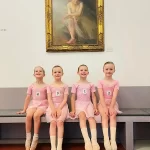 Royal Academy of Dance Exam Success 2025 - 4 young ballerinas sit beneath a painting